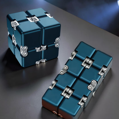 The Curious Mind Unlimited Magic Fidget Cube in dark blue metal, a compact desk toy that folds and unfolds.