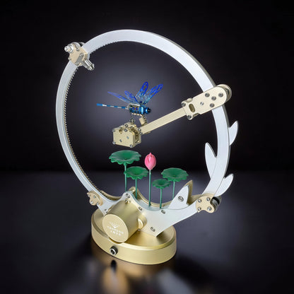 The Curious Mind Flying Dragonfly Kinetic DIY Kit, a metal mechanical model with a blue dragonfly, lotus flowers, and a circular frame.