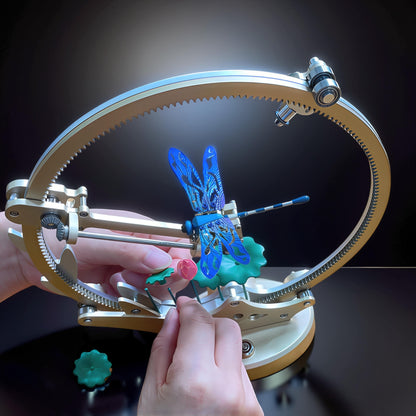 The Curious Mind Flying Dragonfly Kinetic DIY Kit, a metal mechanical model with blue wings and intricate details, shown in a display setting with hands assembling it.