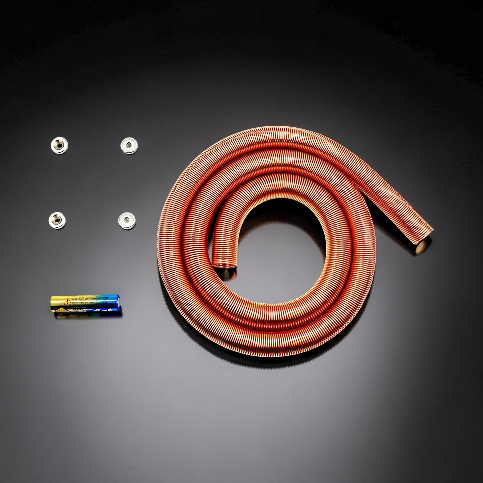 The Curious Mind Electromagnetic Train Puzzle Toy, a copper coil with batteries and metal fasteners on a black background.