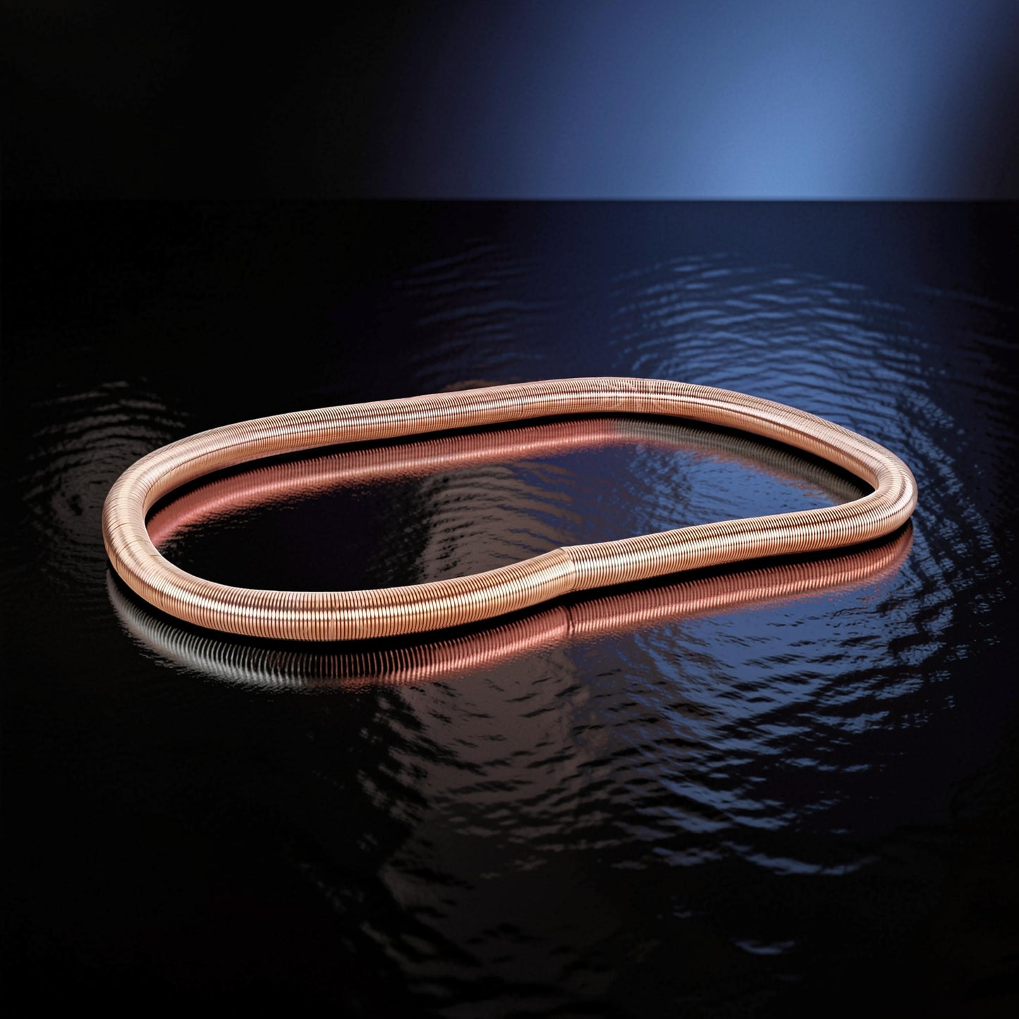 The Curious Mind Electromagnetic Train Puzzle Toy, a copper-colored metal spring in an oval shape on a reflective black surface.