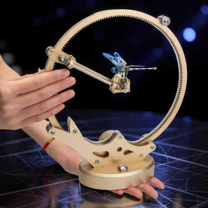 The Curious Mind Flying Dragonfly Kinetic DIY Kit, a metal mechanical model with blue wings and intricate gears, displayed on a circular track.