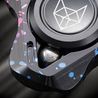 The Curious Mind Spirit Fox Glow Spinner features a black metal body with pink and blue splatter paint accents and a geometric fox logo.