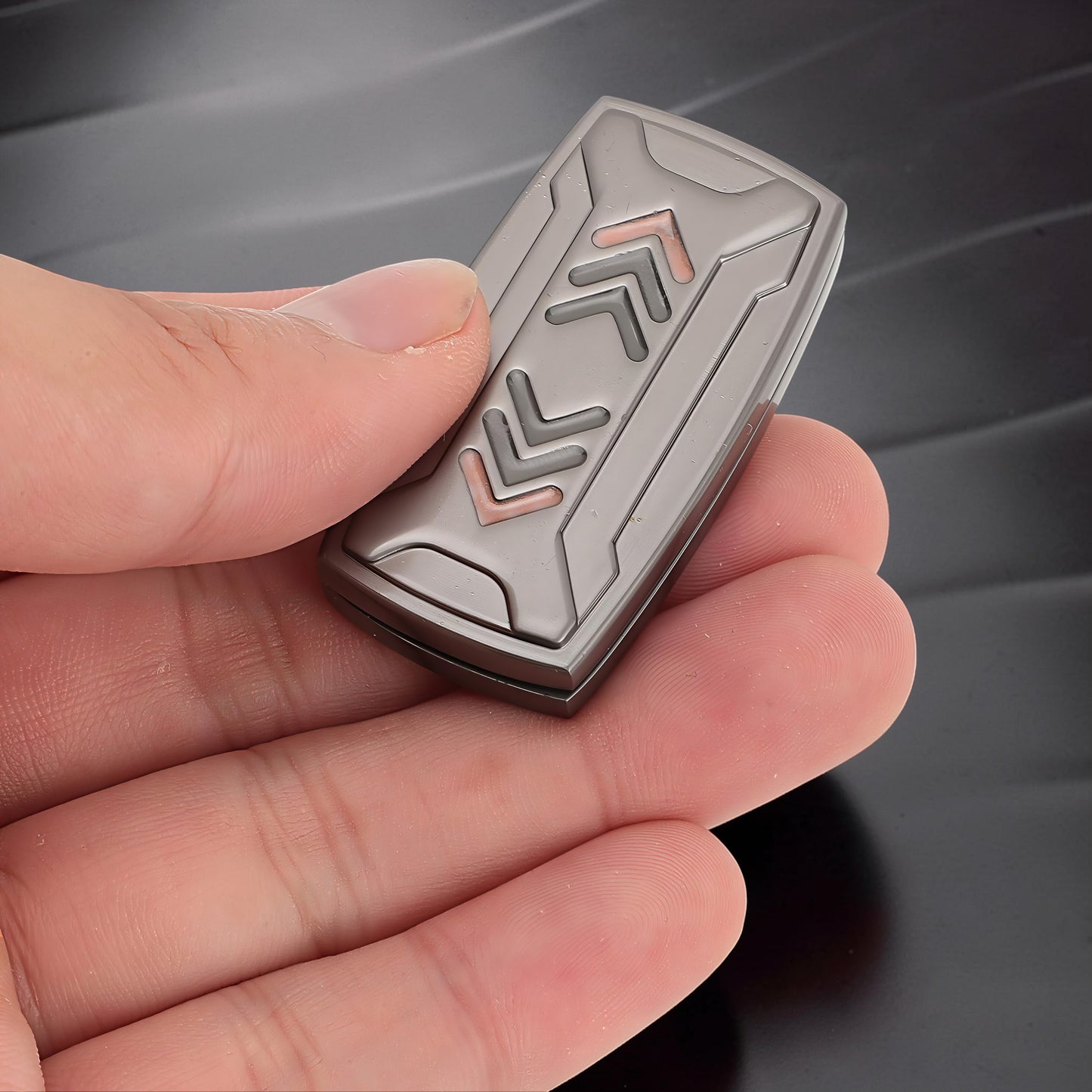 The Curious Mind Arrow Pusher Click Slider fidget toy is grey metal with engraved arrows and copper accents. Compact and tactile for stress relief.