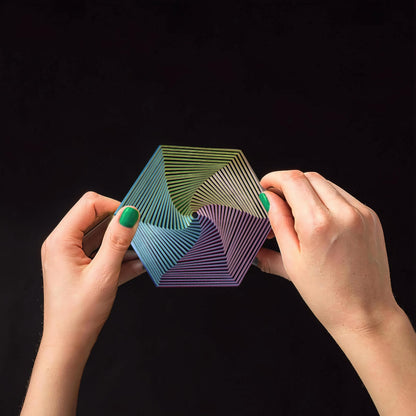 The Curious Mind Hexagon Push Fidget sensory toy with rainbow gradient, held by hands.