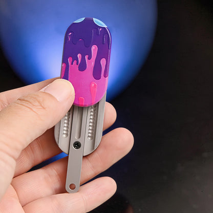 The Curious Mind Ice Cream Push Card Clicker fidget toy with purple and pink dripping icing design. Metal construction.