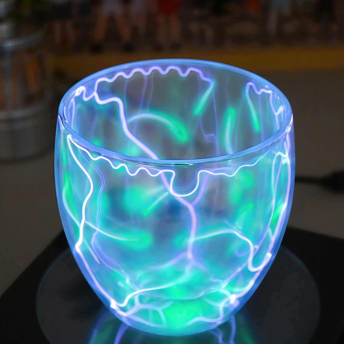The Curious Mind Inert Gas Lightning Cup with display base, featuring swirling blue and green plasma arcs within a glass vessel.