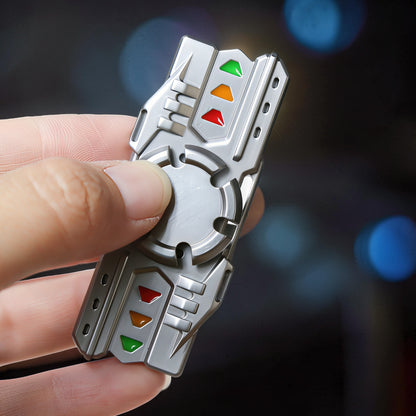 The Curious Mind Laser Cannon Glow Spinner, a metallic grey fidget toy with red, orange, and green accents, held in a hand.