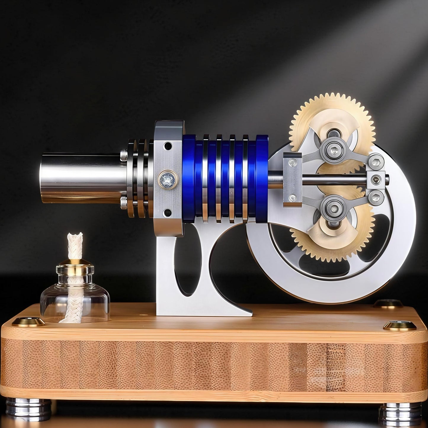 The Curious Mind M20 Stirling engine model with blue and silver metal components on a bamboo base, featuring brass gears and a small fuel burner.