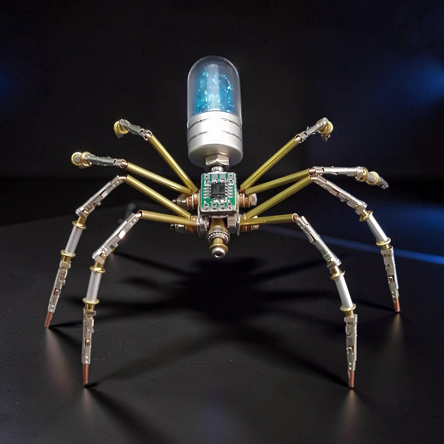 The Curious Mind Style B mechanical spider DIY kit, made of metal with a blue glitter-filled capsule body and circuit board detail.