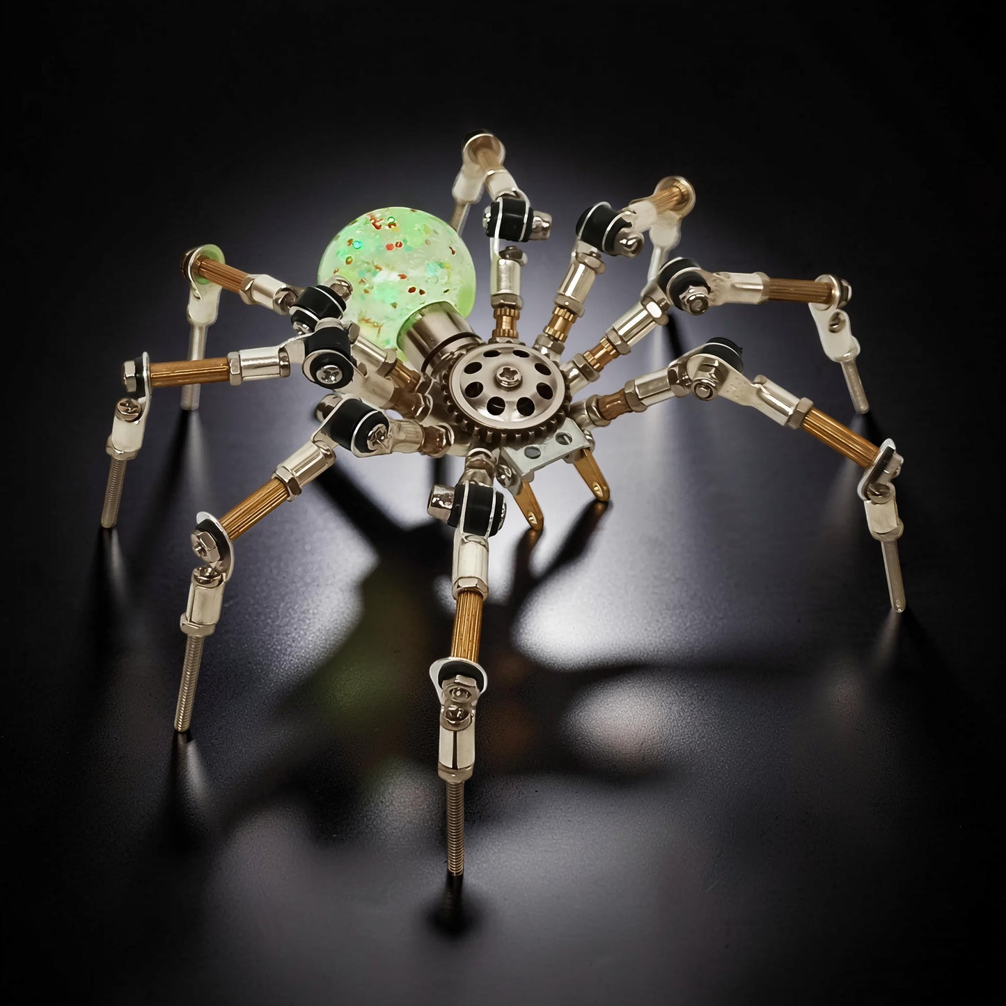 The Curious Mind Style G mechanical spider DIY kit, made of metal with a glowing green orb body.