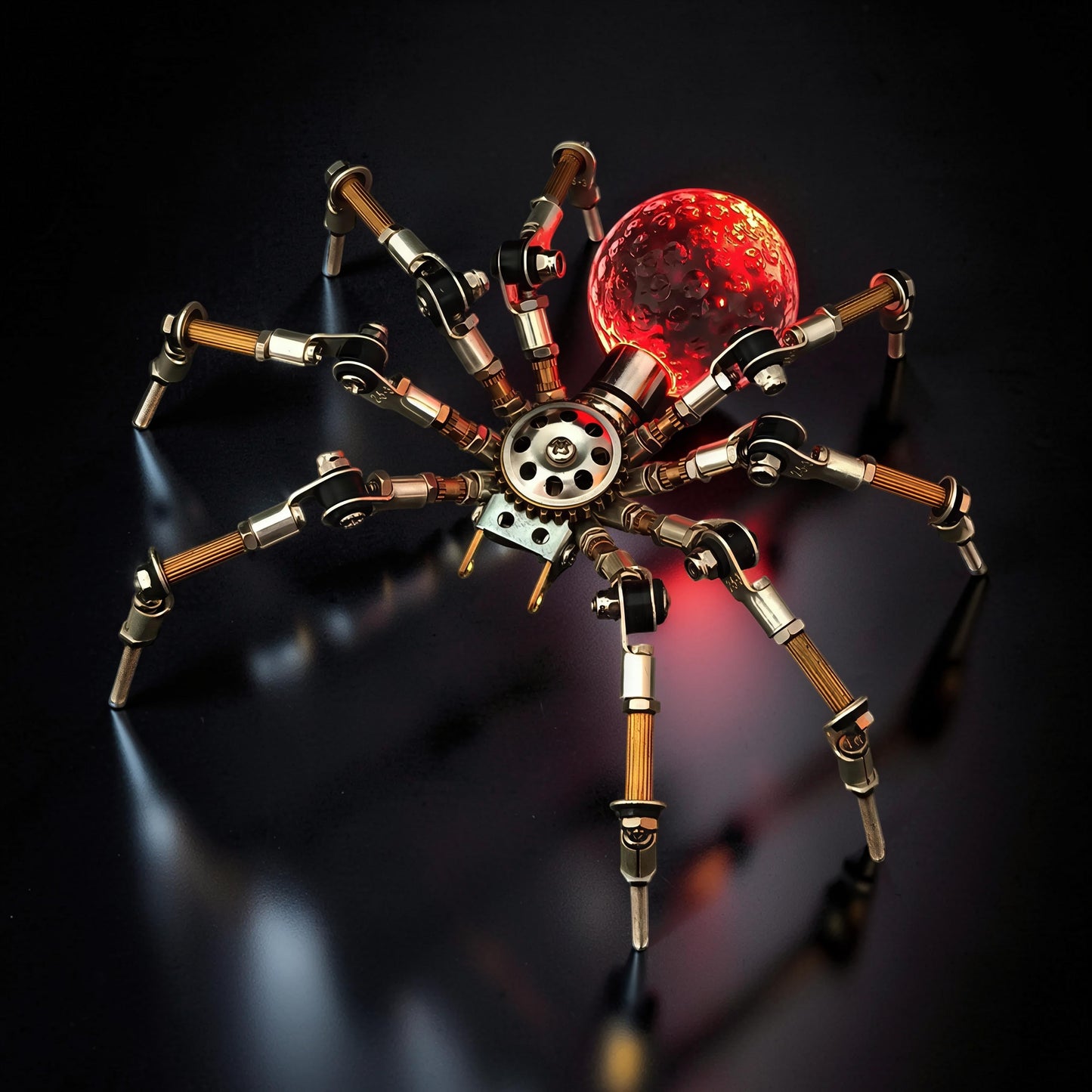 The Curious Mind Style G mechanical spider model kit, made of metal, with a red glowing orb.
