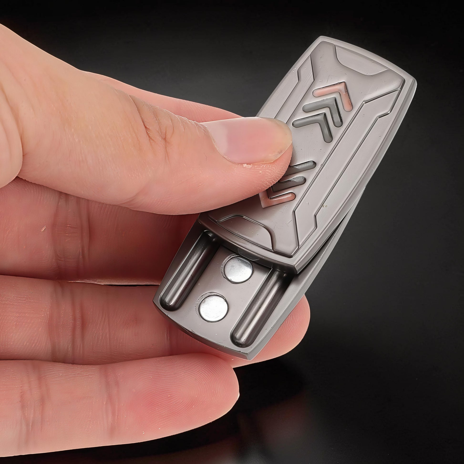 The Curious Mind Arrow Pusher Click Slider fidget toy, made of grey metal with arrow design, held in a hand.