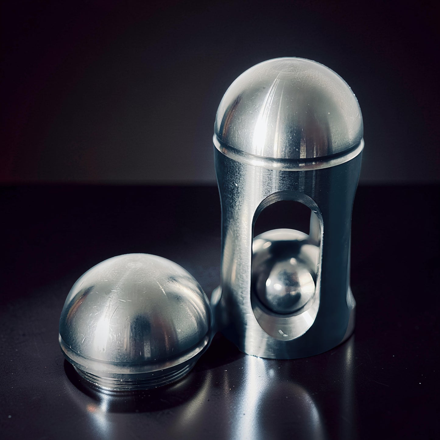 The Curious Mind Hit Egg Pocket Spinner is a compact, metallic fidget toy with a smooth, rounded cap and a cylindrical body featuring an internal ball.