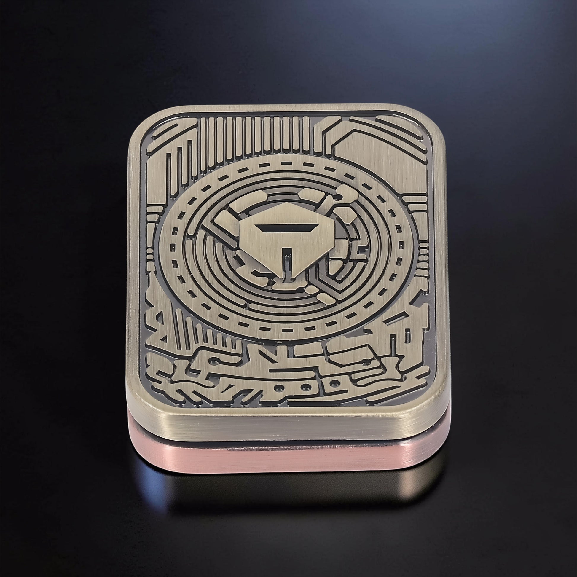 The Curious Mind Three-Body Push Card Fidget, a compact metal fidget toy with a bronze-toned, intricate circuit board design and a central shield emblem.