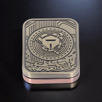 The Curious Mind Three-Body Push Card Fidget, a compact metal fidget toy with a bronze-toned, intricate circuit board design and a central shield emblem.