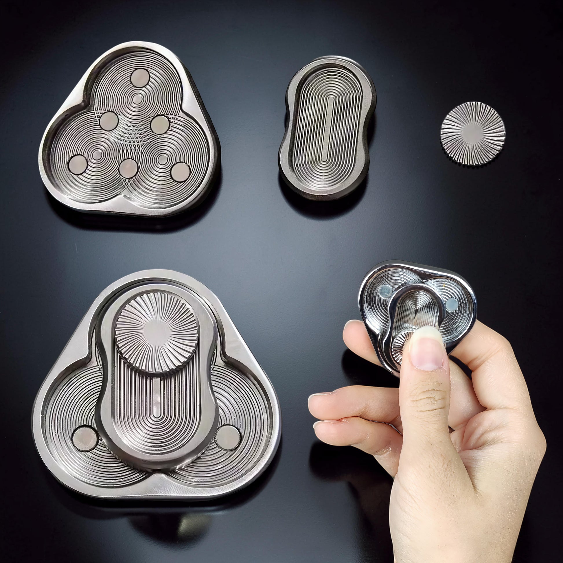 The Curious Mind Triangle Rotary Push Card fidget toy, made of brushed metal with concentric circle detailing and magnetic sliders.