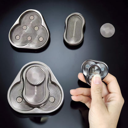 The Curious Mind Triangle Rotary Push Card fidget toy, made of brushed metal with concentric circle detailing and magnetic sliders.