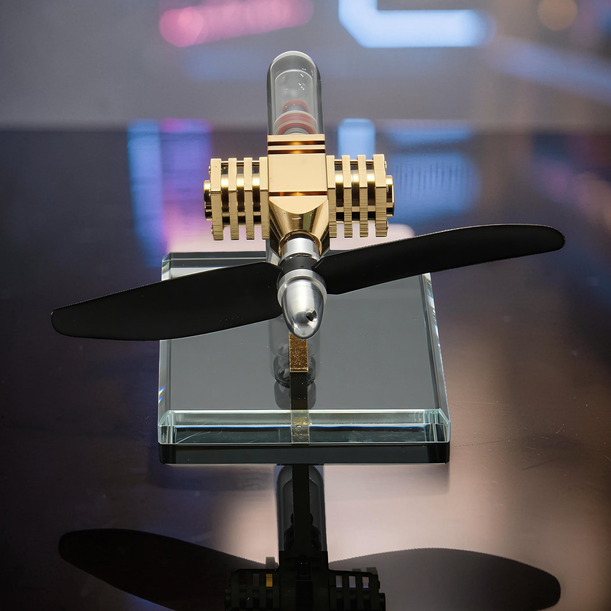 The Curious Mind Mini Aircraft Stirling Engine Display Model, gold and silver metal with black propeller on glass base.
