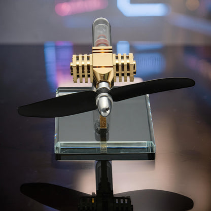 The Curious Mind Mini Aircraft Stirling Engine Display Model, gold and silver metal with black propeller on glass base.