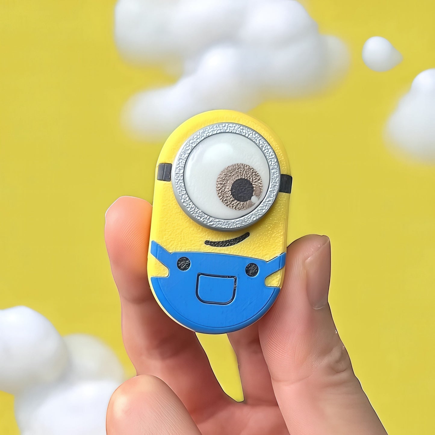The Curious Mind Minion Pocket Push Pop Clicker fidget toy, yellow and blue metal and plastic, with one large eye and blue overalls.