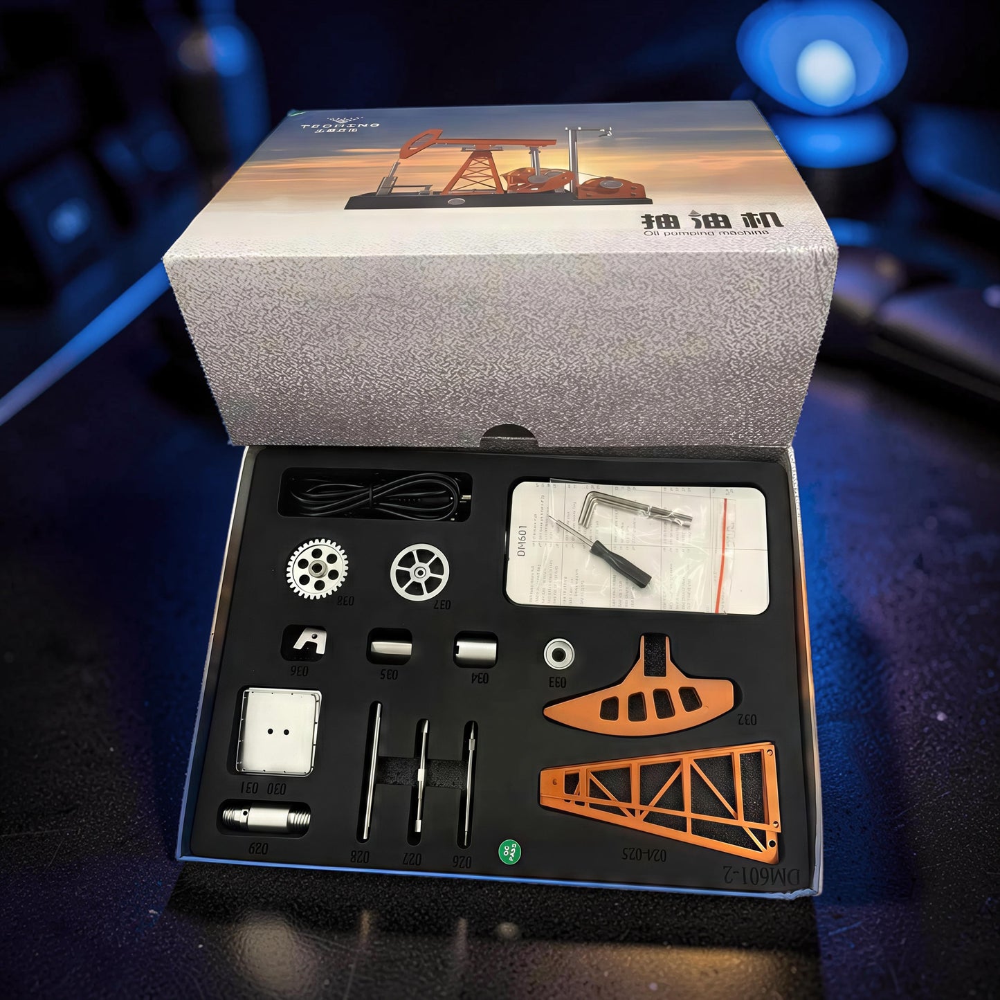 The Curious Mind Oil Derrick Pumping Unit DIY Kit, a metal mechanical model kit with orange and silver parts, gears, and tools.