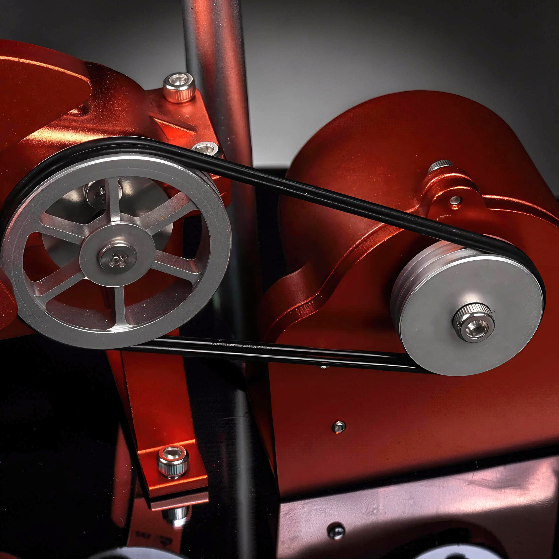 The Curious Mind Oil Derrick Pumping Unit DIY Kit features a metal construction with a red metallic finish and a black drive belt connecting silver pulleys.