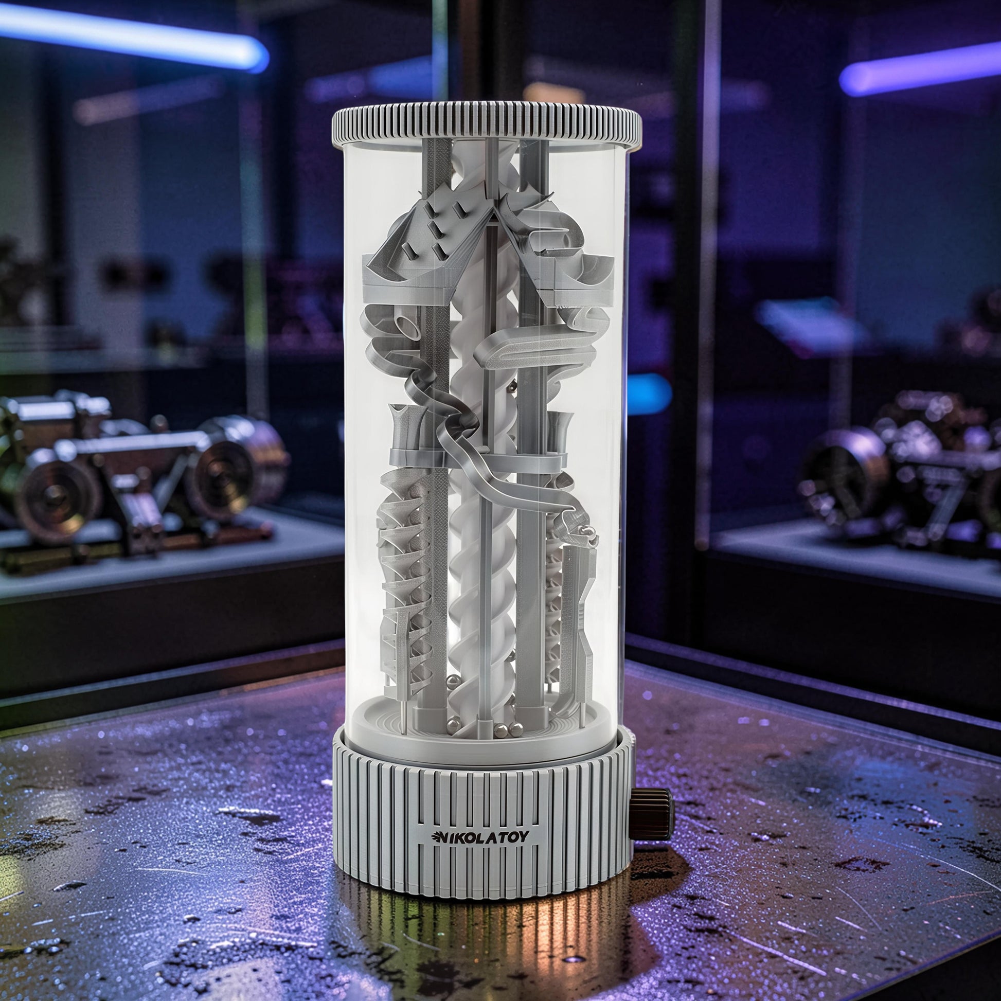 The Curious Mind Spinning Pinball RGB Night Light features a grey PLA construction with a clear cylinder, showcasing intricate tracks and balls. It has a ribbed base with a dial and emits ambient light.
