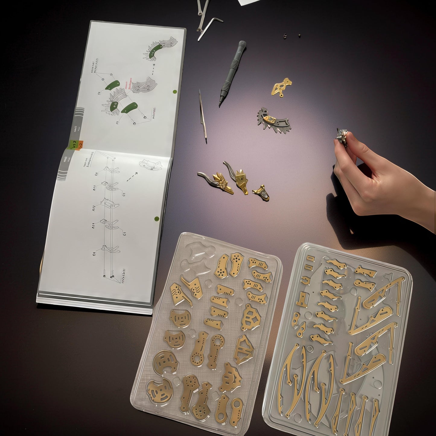 The Curious Mind Pterosaur DIY Kit with metal parts laid out next to instructions and tools. A hand holds a small assembled piece.
