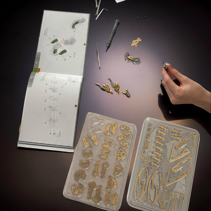 The Curious Mind Pterosaur DIY Kit with metal parts laid out next to instructions and tools. A hand holds a small assembled piece.