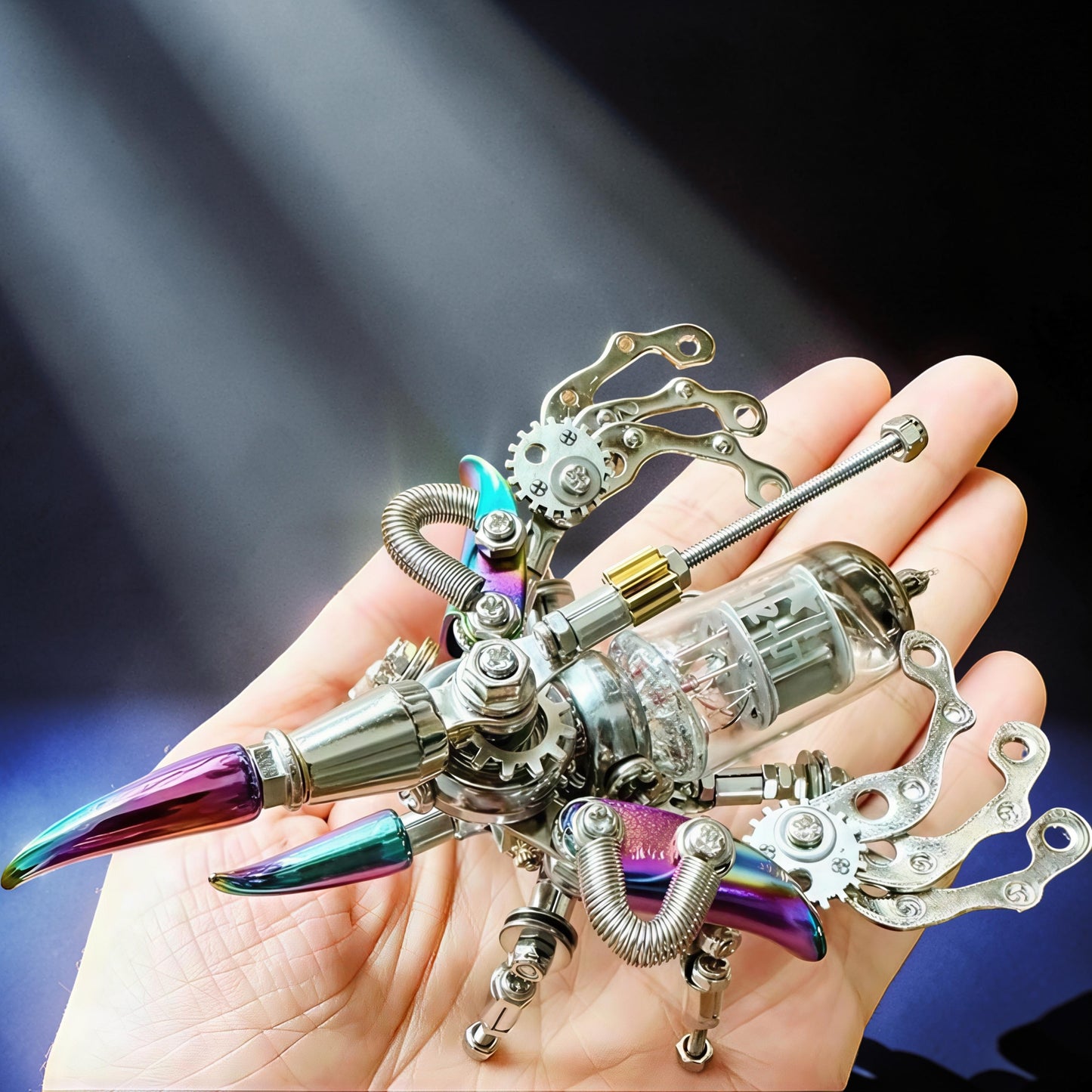 The Curious Mind Punk Beetle 3D metal model kit, steampunk insect with iridescent accents and glass tube body, held in a hand.