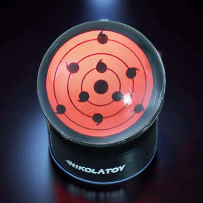 The Curious Mind Sharingan Crystal Ball Decorative Ornament, a red and black orb with concentric circles and tomoe symbols on a black base.