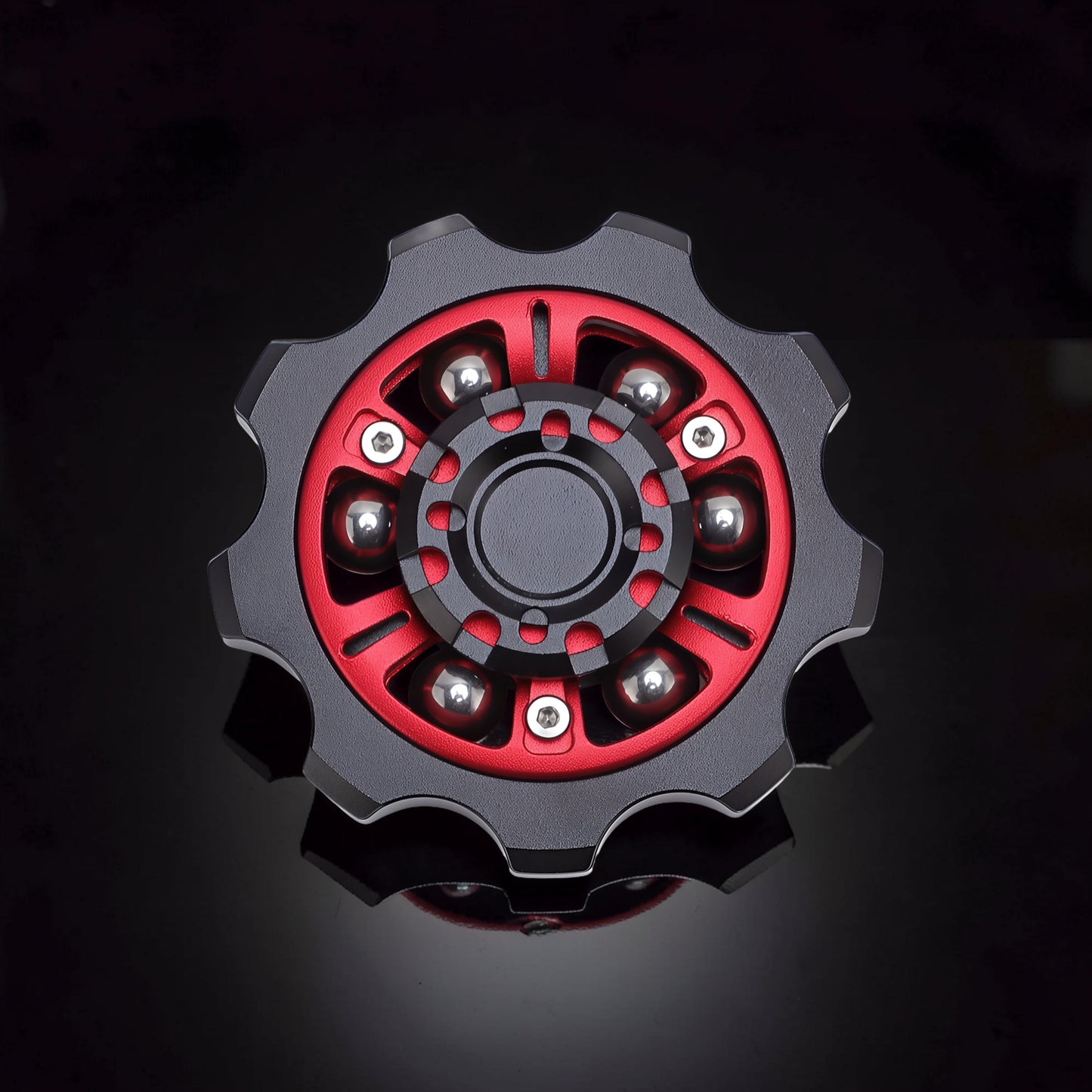The Curious Mind Six-Bead Gear Spinner in black and red metal with six silver ball bearings. Gear-shaped design.