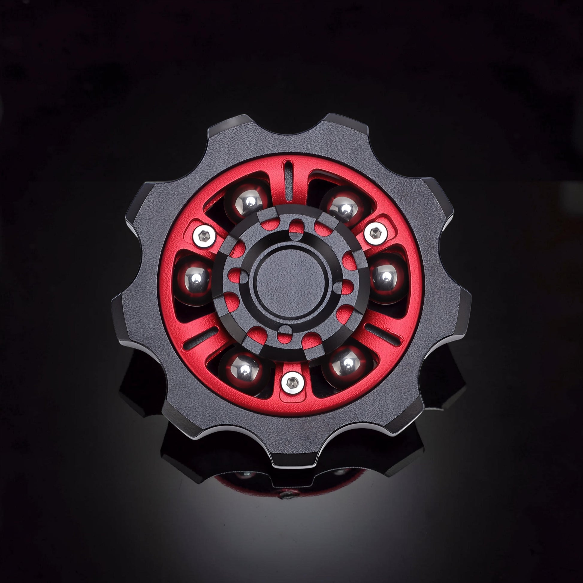 The Curious Mind Six-Bead Gear Spinner in black and red metal with six silver ball bearings. Gear-shaped design.