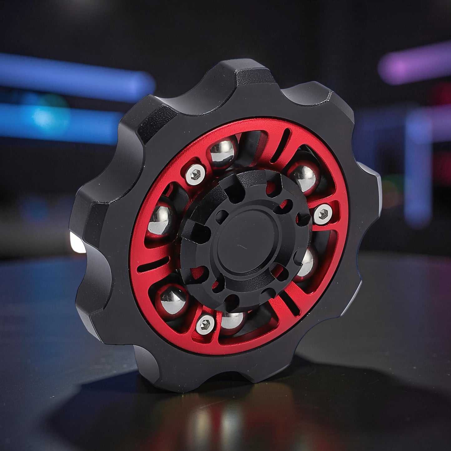 The Curious Mind Six-Bead Gear Spinner: black and red metal fidget toy with six silver ball bearings and gear-like outer edge.