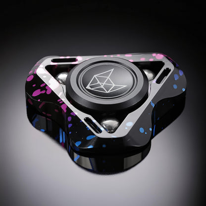 The Curious Mind Spirit Fox Glow Spinner features a black metal body with pink and blue splatter accents and a central fox logo.