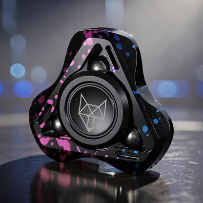 The Curious Mind Spirit Fox Glow Spinner is a black metal fidget spinner with pink and blue splatter details and a fox logo.