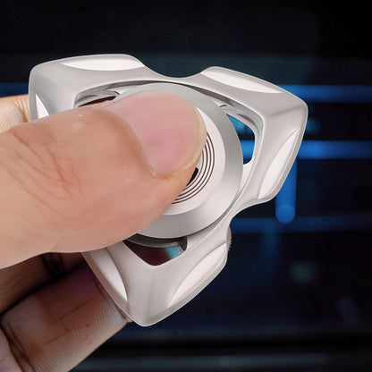 The Curious Mind stainless steel tri-blade spinner held by a thumb and finger. Features a sleek, metallic silver finish and a balanced profile for smooth rotation.