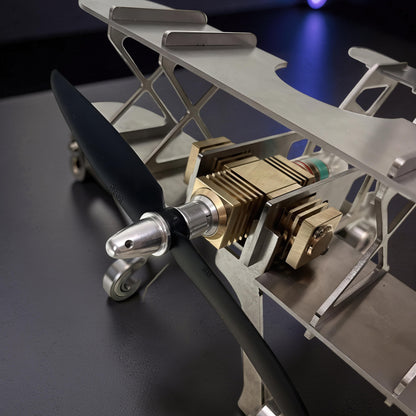 The Curious Mind Stirling Engine Model Aircraft, a metal biplane model with brass engine details and a black propeller, perfect for desktop display.