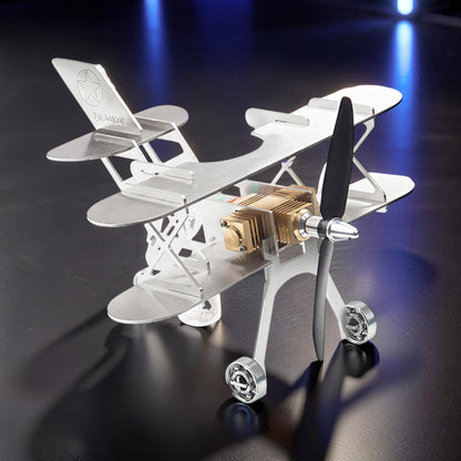 The Curious Mind Stirling Engine Model Aircraft, a silver metal biplane with a gold engine and black propeller, on display.