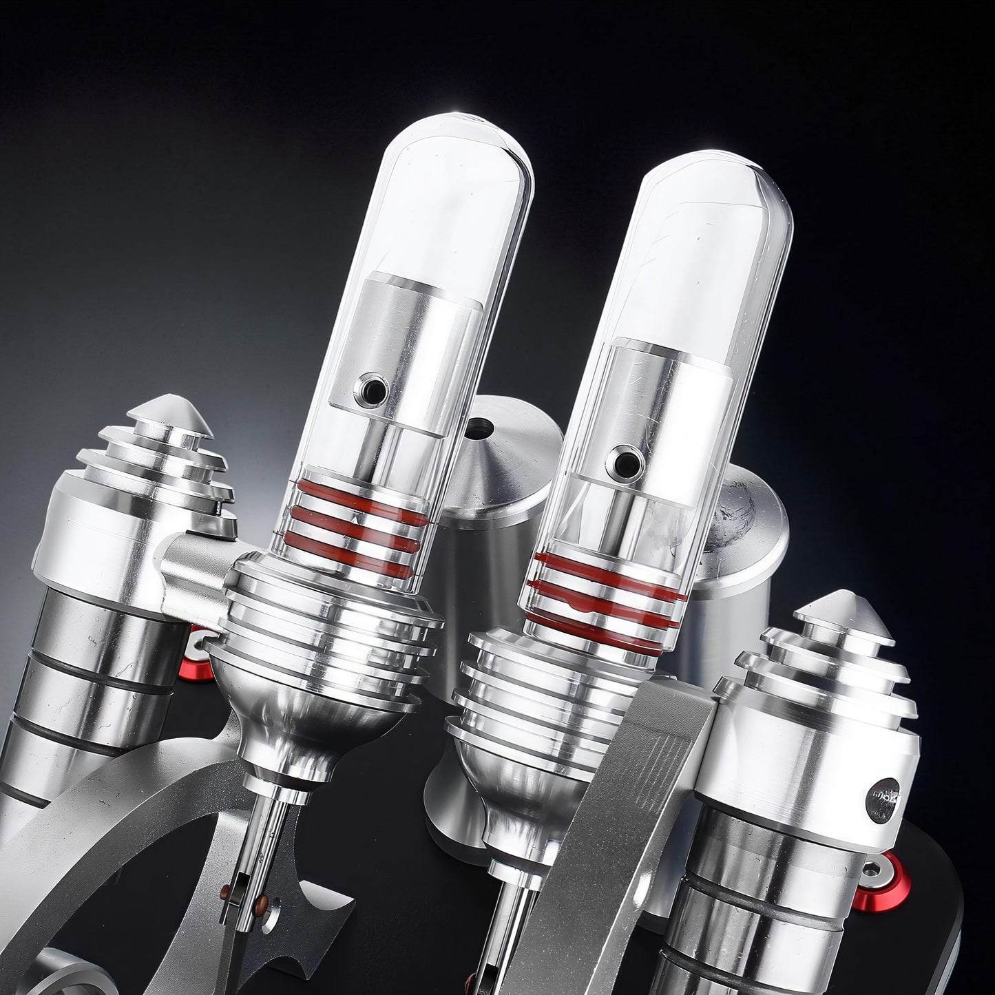 The Curious Mind Stirling Engine V4 Display Model, a metal mechanical model with clear cylinders and red accents, showcasing intricate engineering.