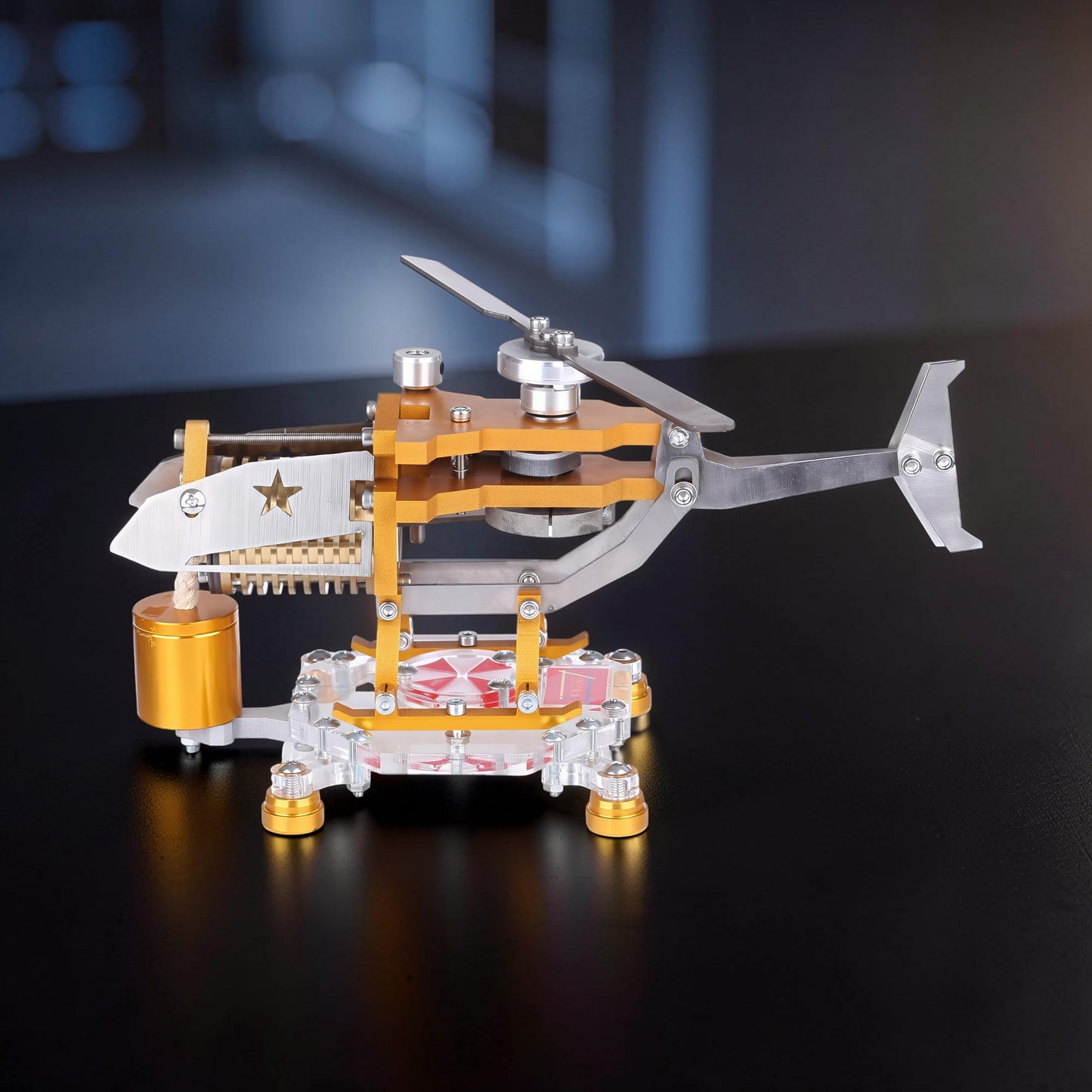 The Curious Mind Fire-Absorbing Stirling Helicopter Model, a metal desktop display engine with gold and silver accents, featuring a star emblem.