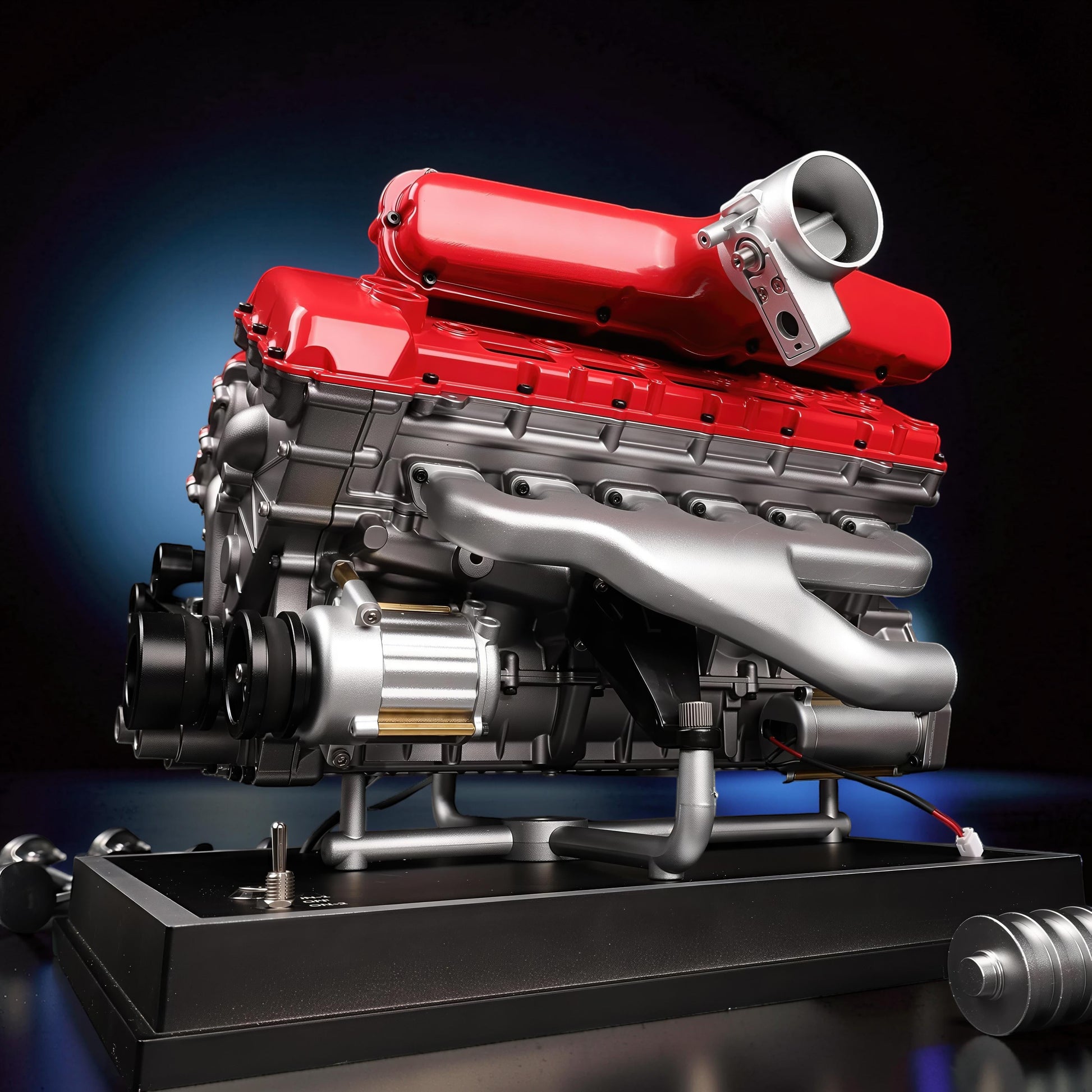 The Curious Mind V12 car engine model kit, a detailed metal replica with red and silver components, displayed on a black base.