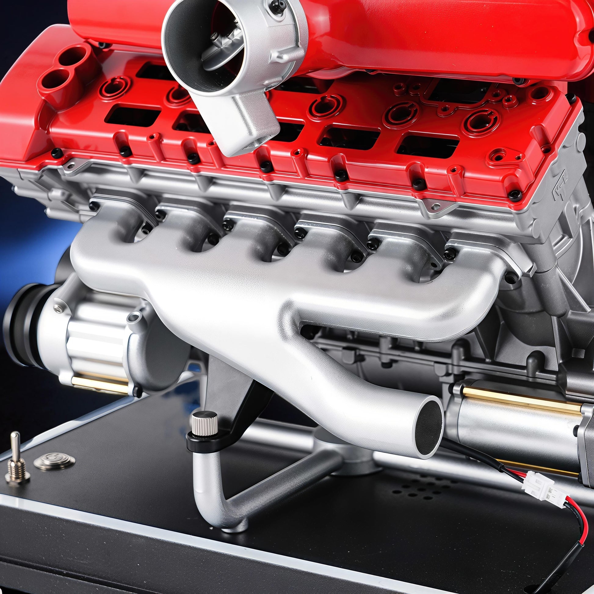 The Curious Mind V12 car engine DIY kit, a detailed metal model with red and silver components, mounted on a black display base.