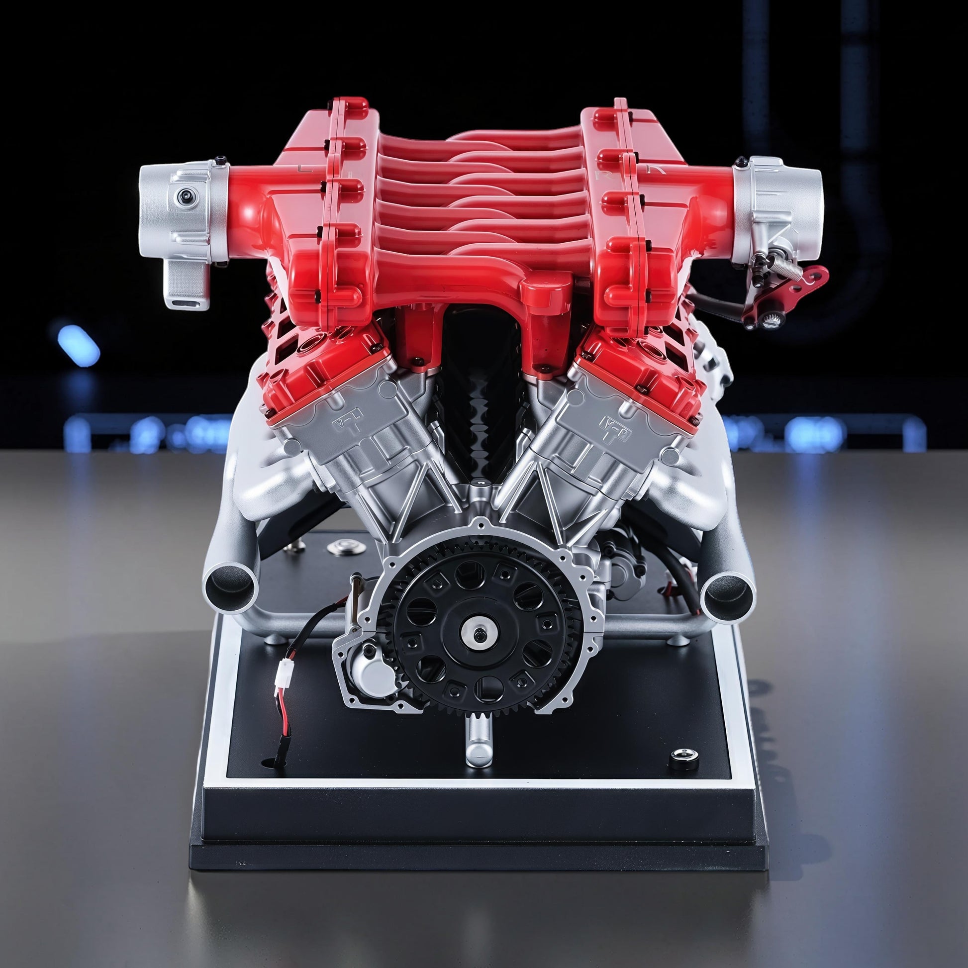 The Curious Mind V12 Car Engine DIY Kit, a detailed metal model with red and silver components on a black display base.