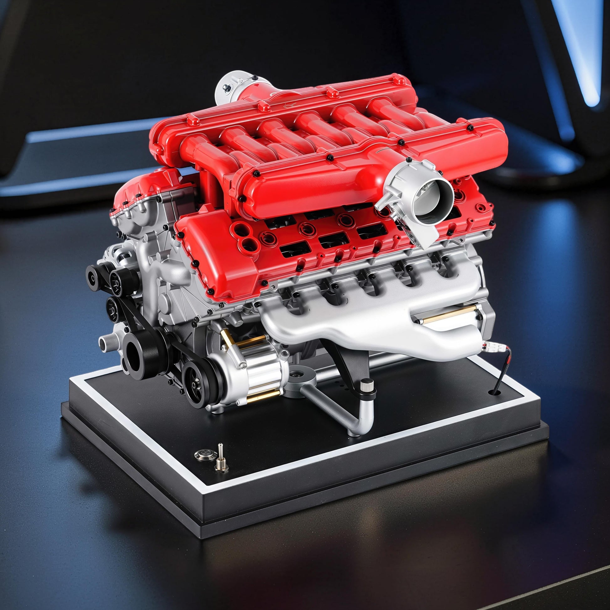 The Curious Mind V12 car engine model kit, red and silver metal construction, displayed on a black base.