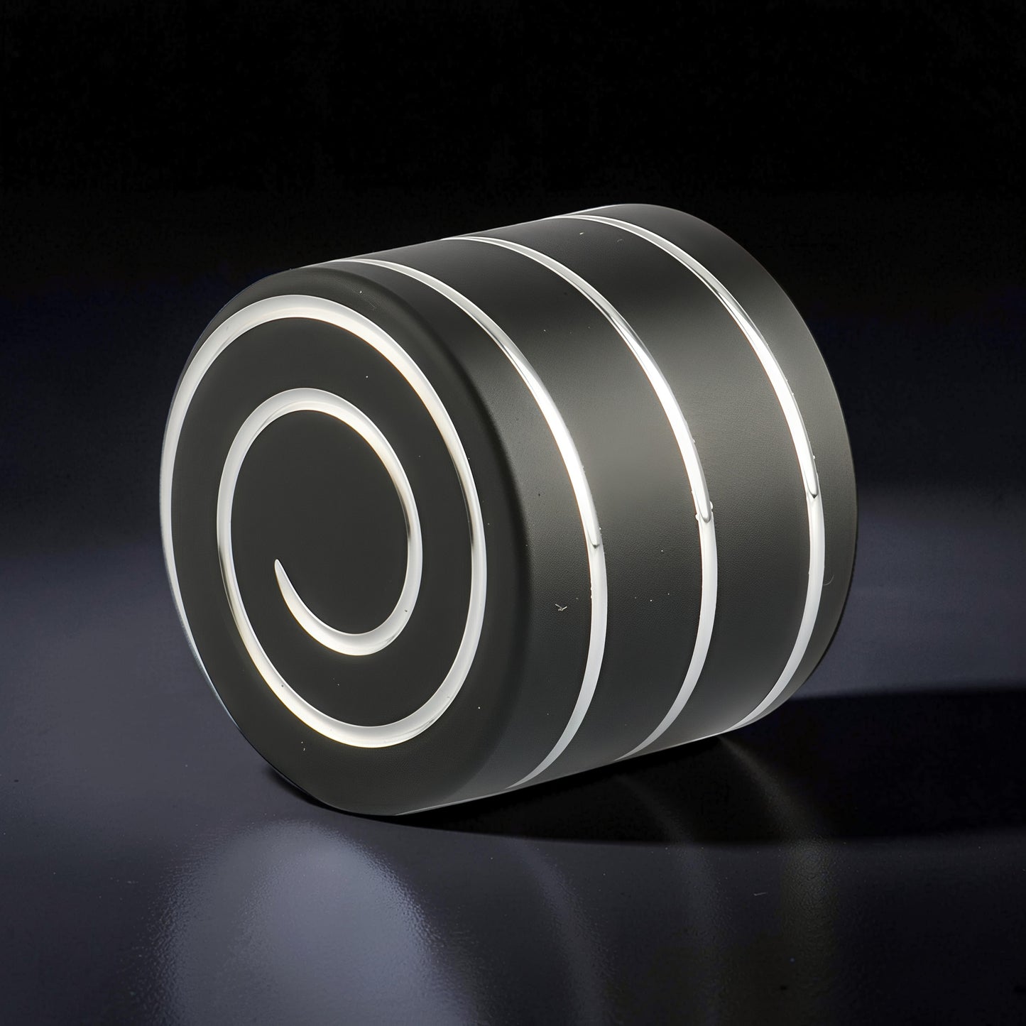 The Curious Mind Vortecon kinetic desk spinner, a weighted metal cylinder with a matte black finish and a white spiral design.