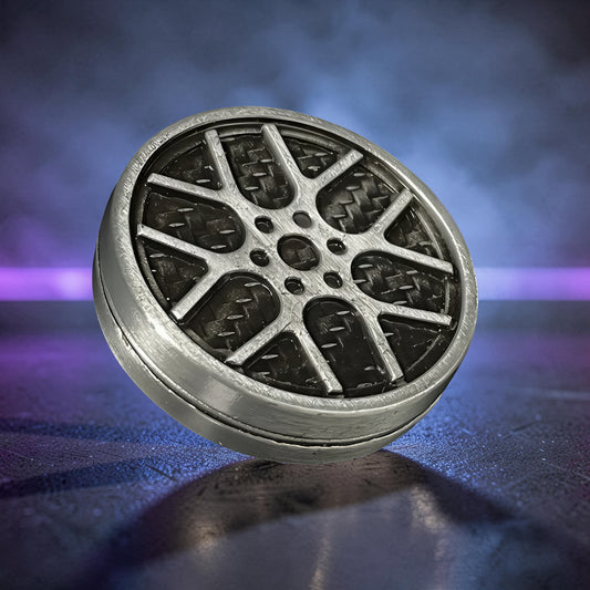 The Curious Mind Wheel Hub Coin Clicker fidget toy, silver metal with a car wheel design and carbon fiber texture.