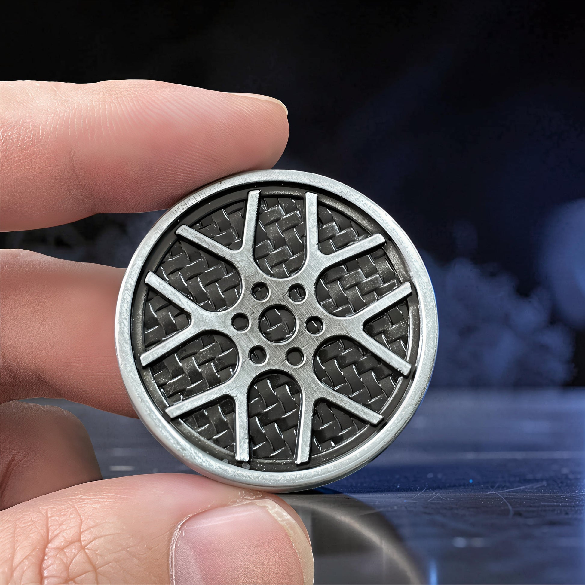 The Curious Mind Wheel Hub Coin Clicker fidget toy, silver metal with a carbon fiber pattern and wheel spoke design.