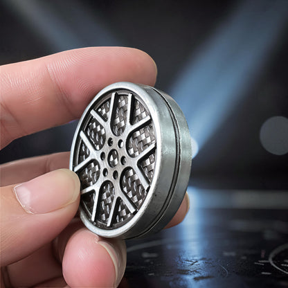 The Curious Mind Wheel Hub Coin Clicker fidget toy, silver metal with a detailed car wheel design, held in a hand.
